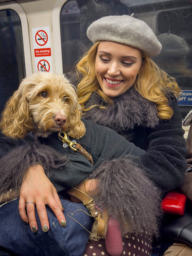 a woman in a grey beret sites on the tube with a dog on her lap