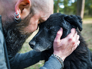 Man embracing his old black dog outside.