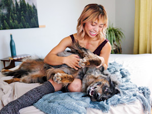 Woman snuggling a dog in her bed at home.