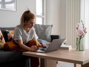 Young woman in online call sitting on couch in her living room on laptop