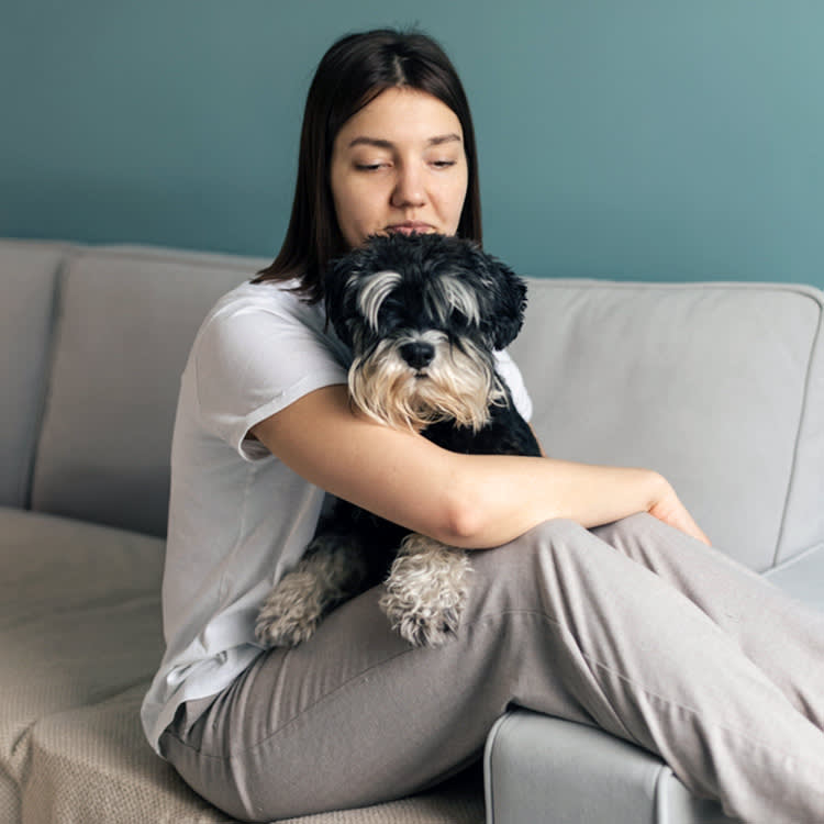 Woman sitting on couch, frustrated with her small dog.