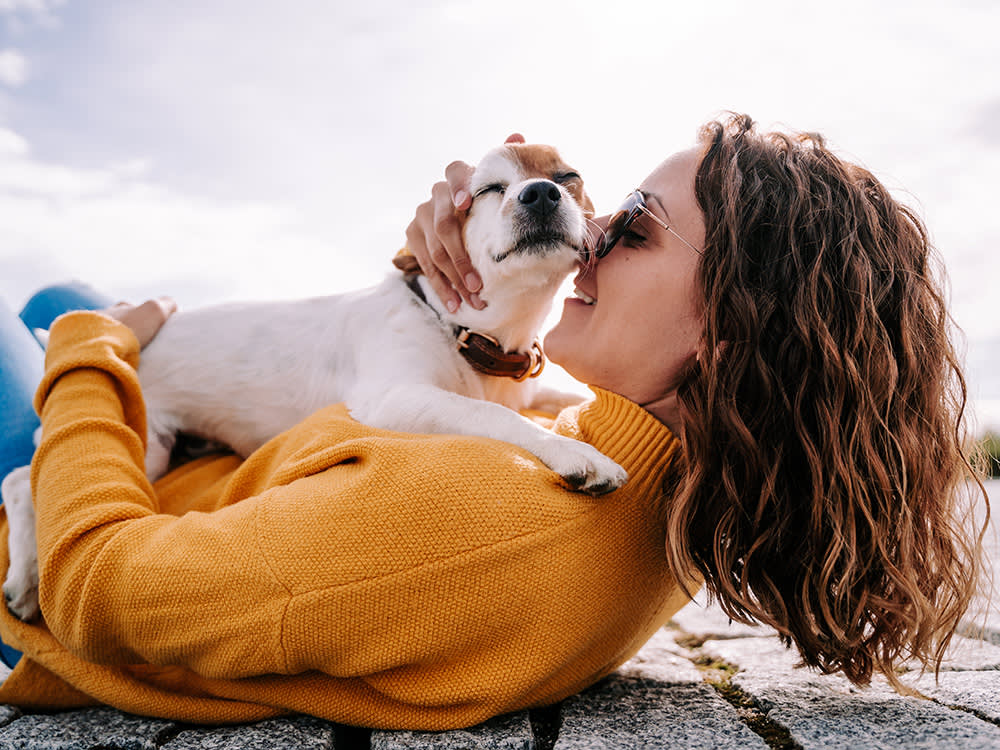 A beautiful woman lying down in the park hugging her cute little dog.