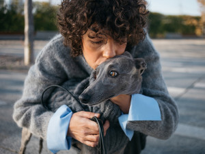 A woman in a parking lot kissing her dog. 