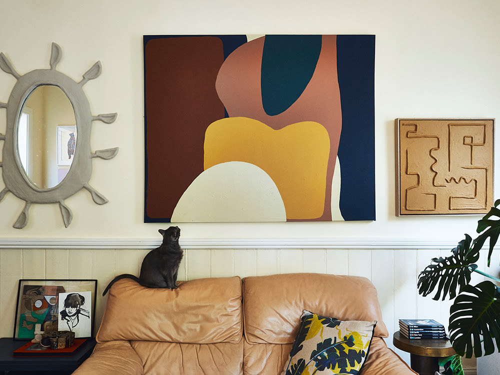 Black cat sitting on top of a leather sofa staring up at an abstract painting in a modern living room