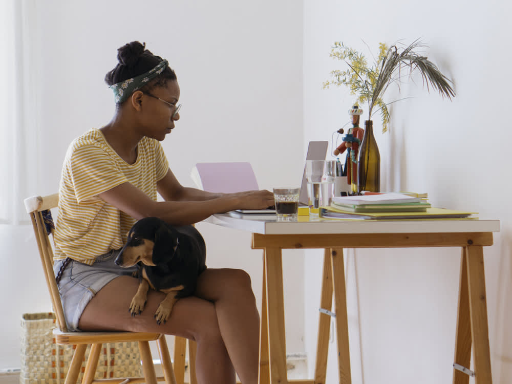 A woman working at her desk with a dog sitting on her lap. 