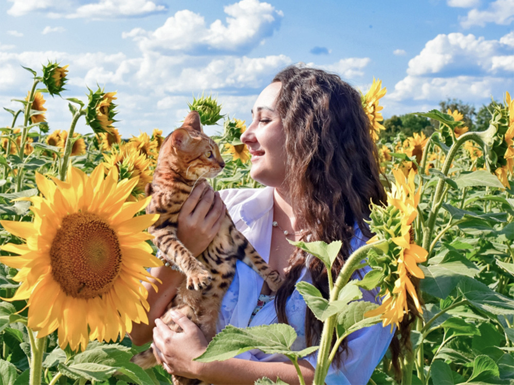 Woman holding her cat in a sunflower field outside.