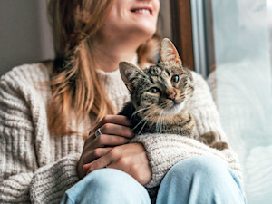 Woman holding cat in her lap at home.