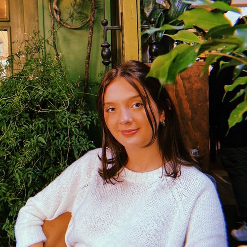 Casual headshot of a young woman with dark shoulder length hair against a background of plants.}}