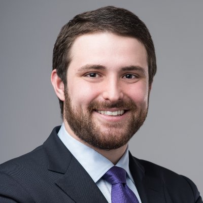 Formal headshot of a white man with a beard, suit, and purple tie.}}