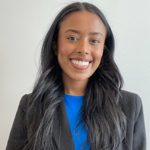 Formal headshot of a young woman in a suit smiling at the camera.}}