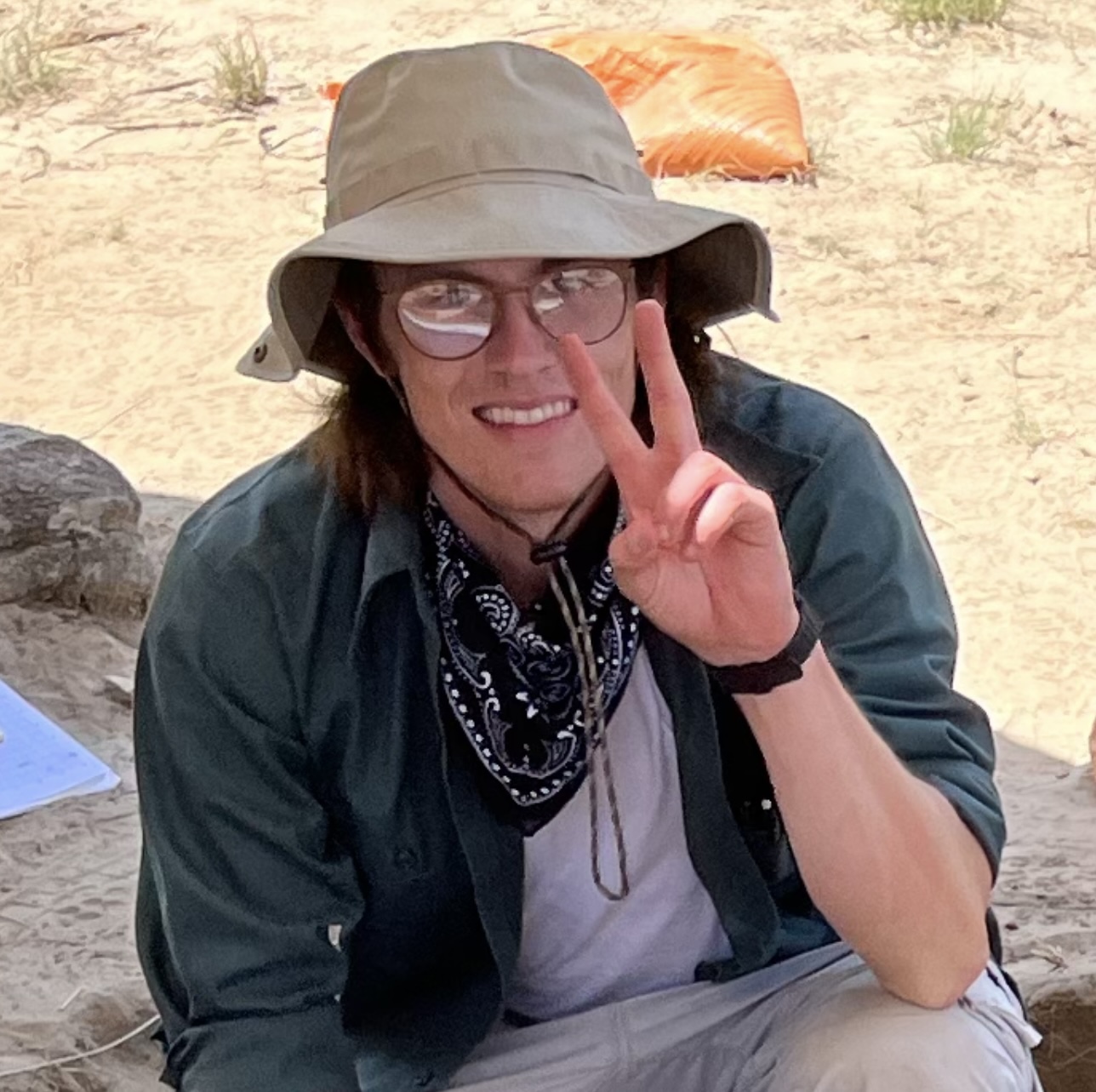 young man in hiking clothes making a peace sign with one hand}}