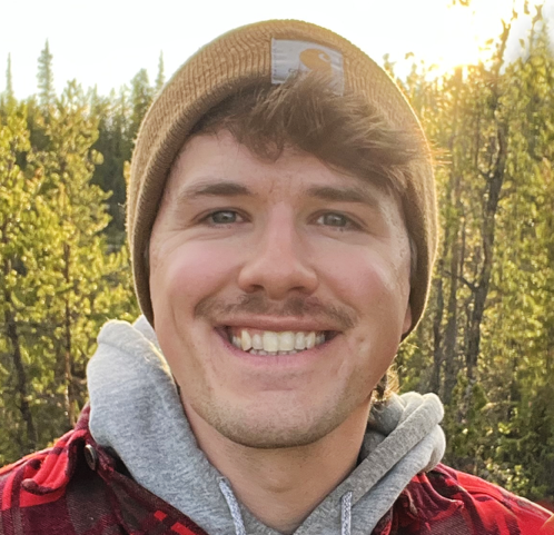 A photo of Thomas Gagnon-van Leeuwen, a white man wearing a brown beanie and plaid shirt in the woods.}}