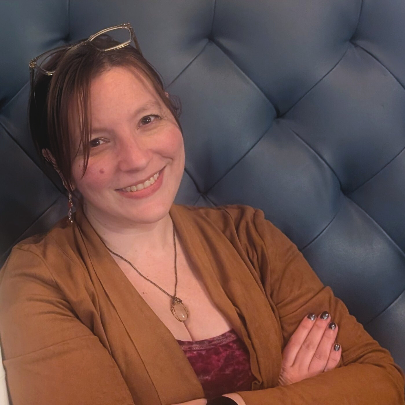 Casual headshot of a smiling woman with glasses on her head and her arms crossed leaning slightly to one side.}}