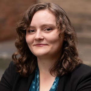Headshot of a young white woman with curly hair smiling at the camera.}}