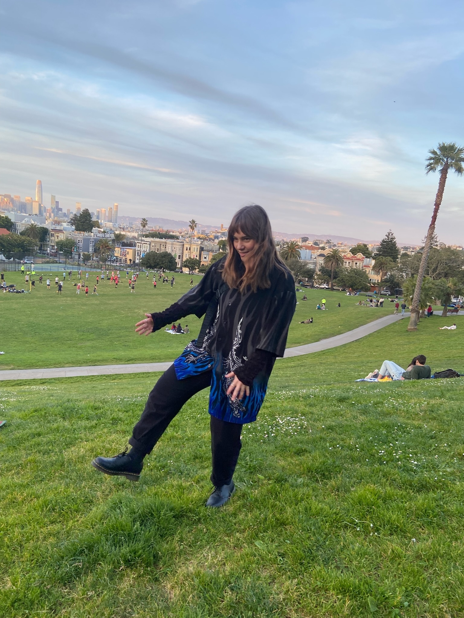 Young white woman standing on one leg in a park with the San Francisco skyline in the background.}}
