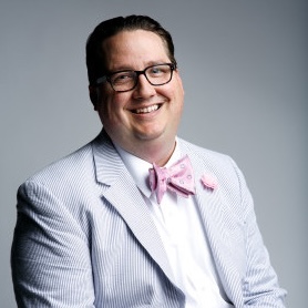 A white man in a suit and bowtie smiling broadly.}}
