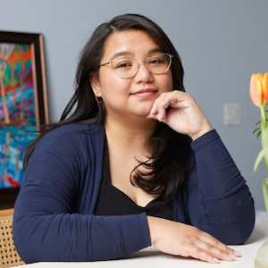 Head and shoulders shot of a young woman at a desk with her chin rested on one hand.}}