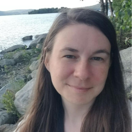casual headshot of woman with a lake and trees in the background}}