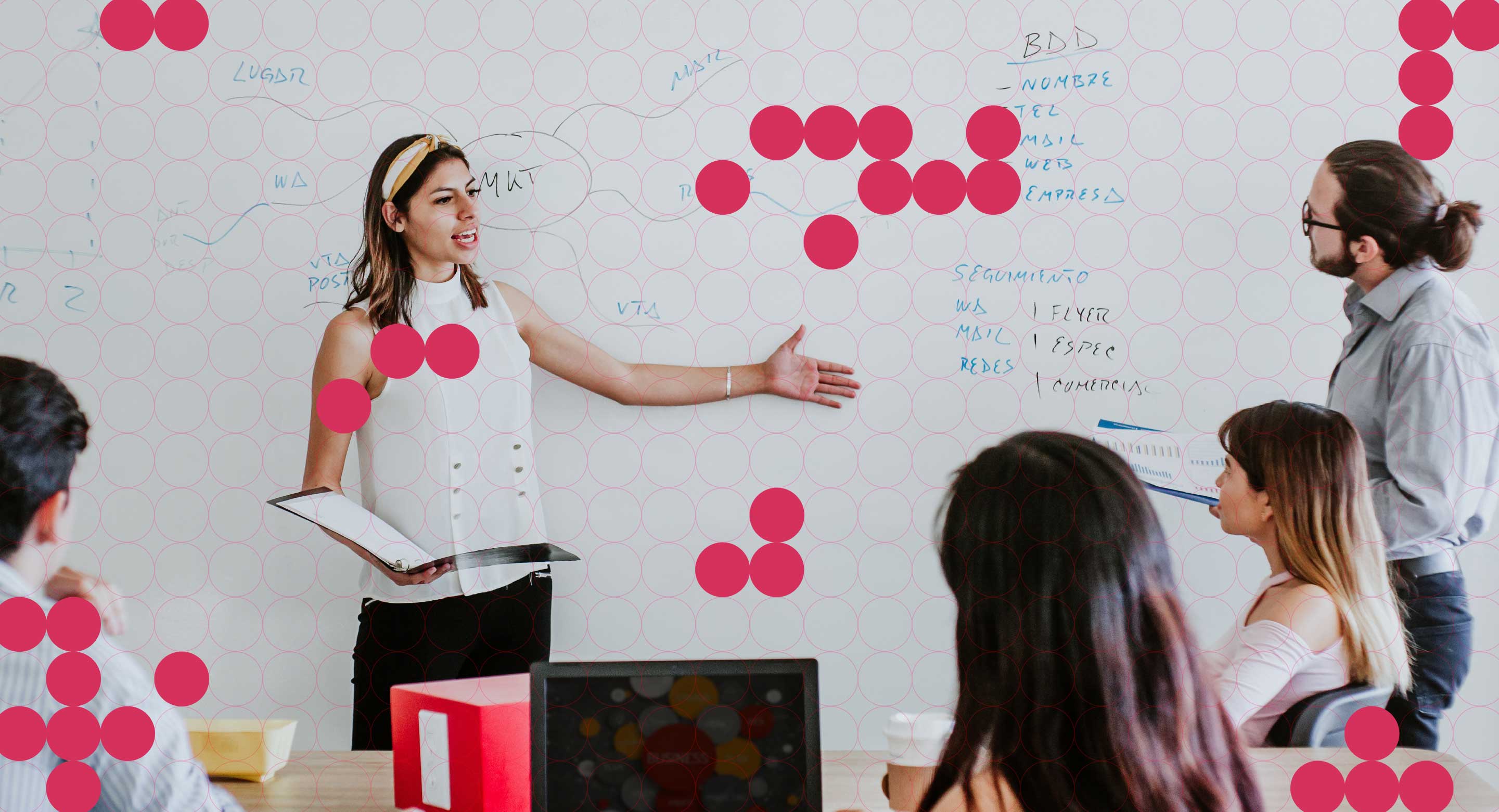 A photo of a woman standing in front of a white board presenting to her team with colourful dot graphics overlaying the image.
