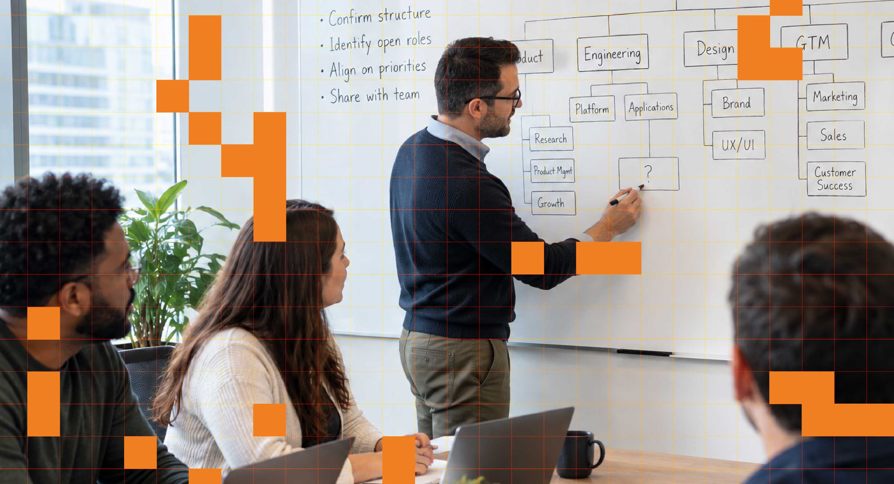 A man works at a whiteboard in front of a board room of colleagues.