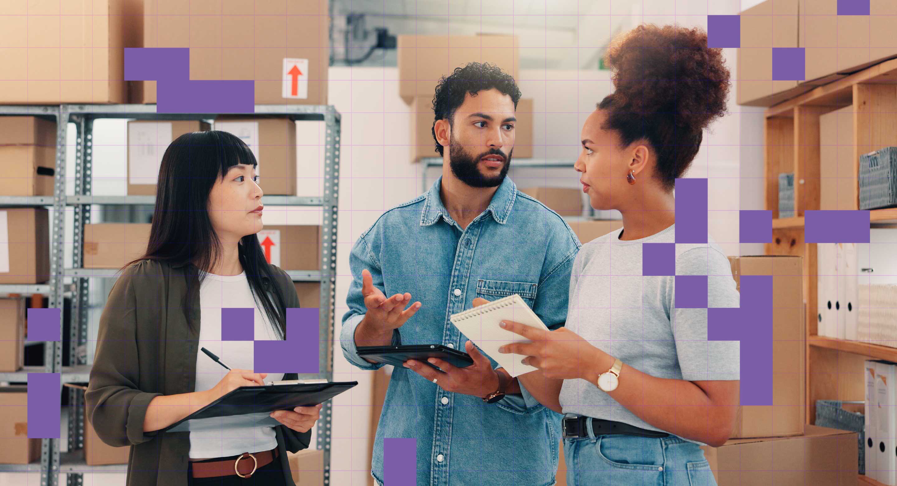 Three coworkers stand in a back room with boxes discussing something.