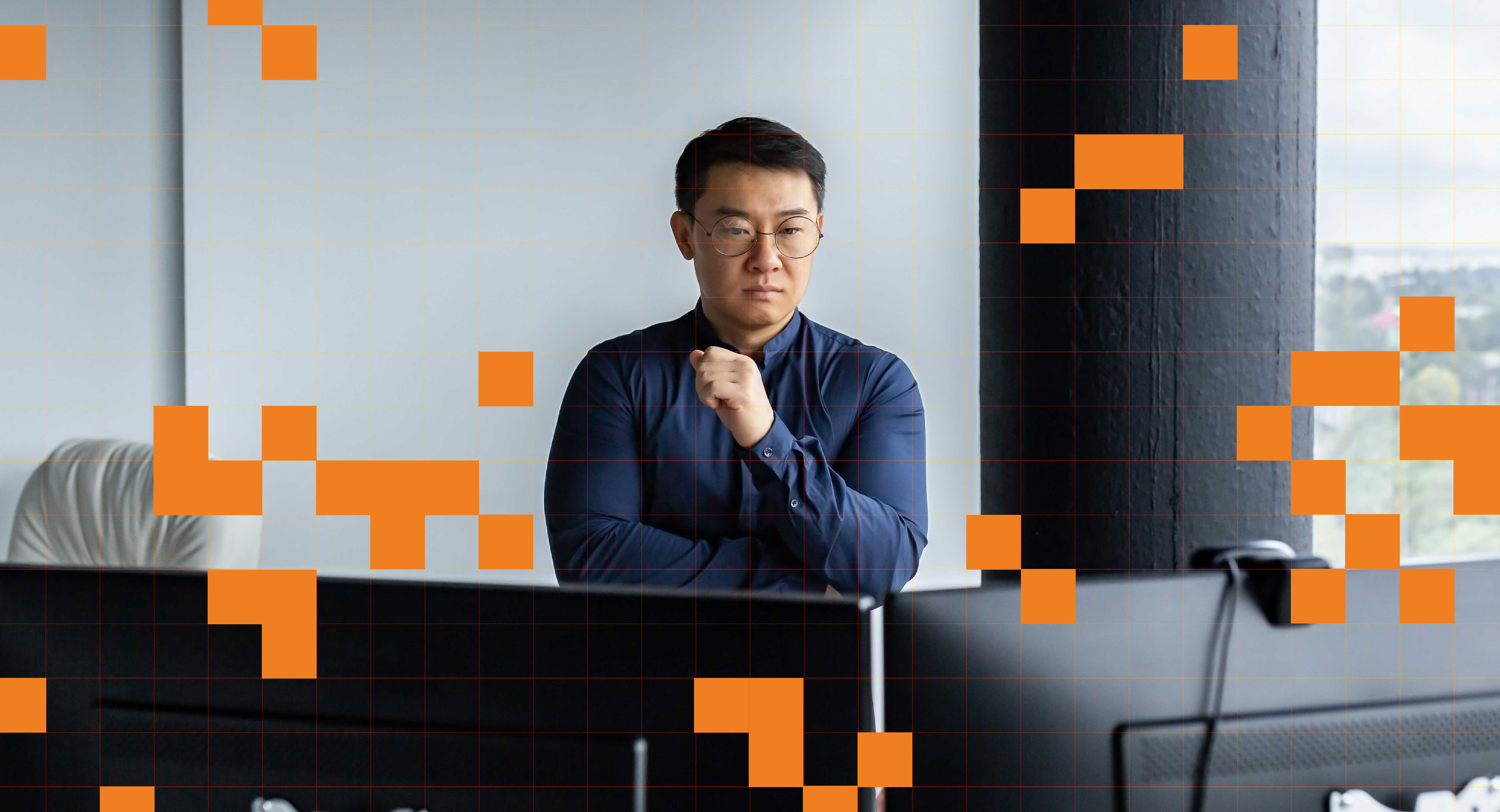 A person stands in front of two computer screens, assessing.