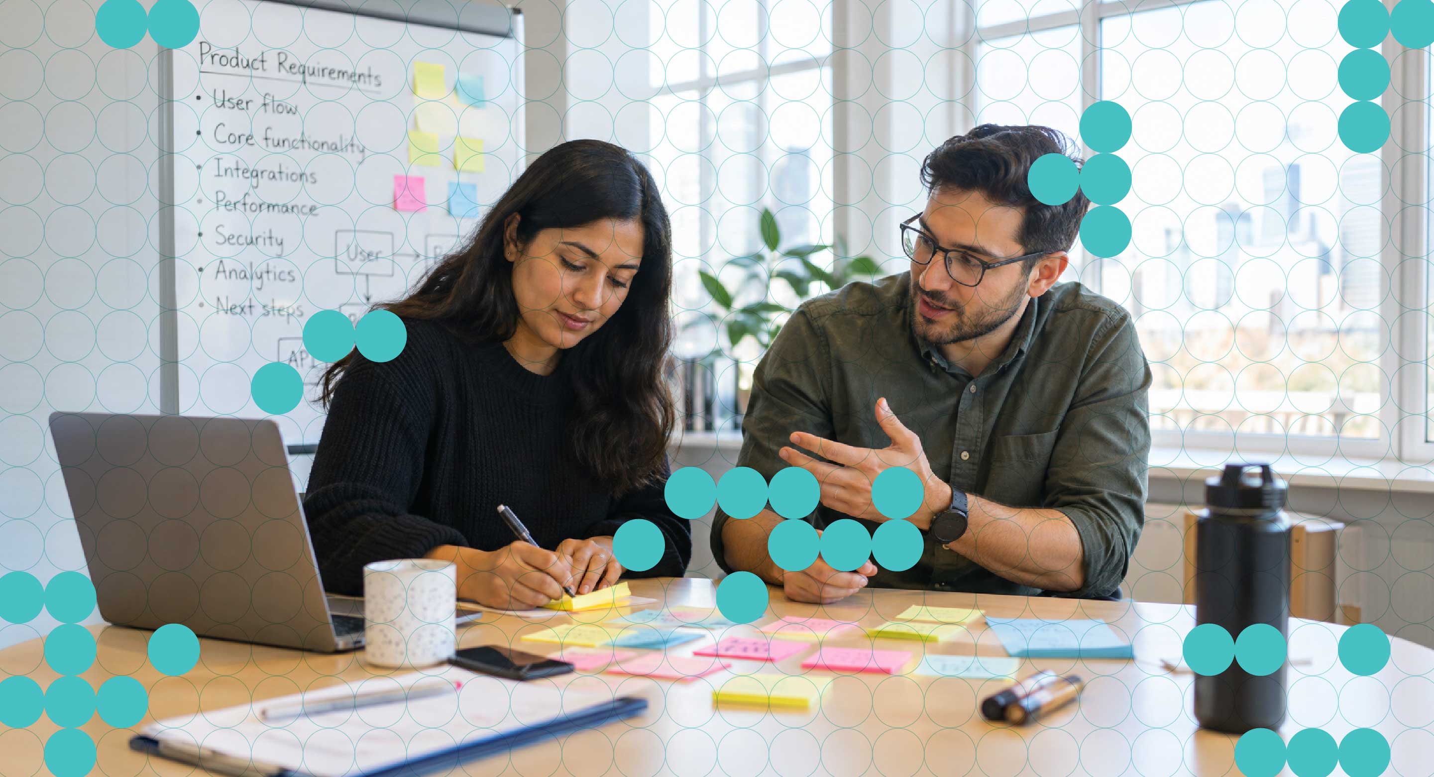 Two colleagues collaborate at a desk in an office meeting room.