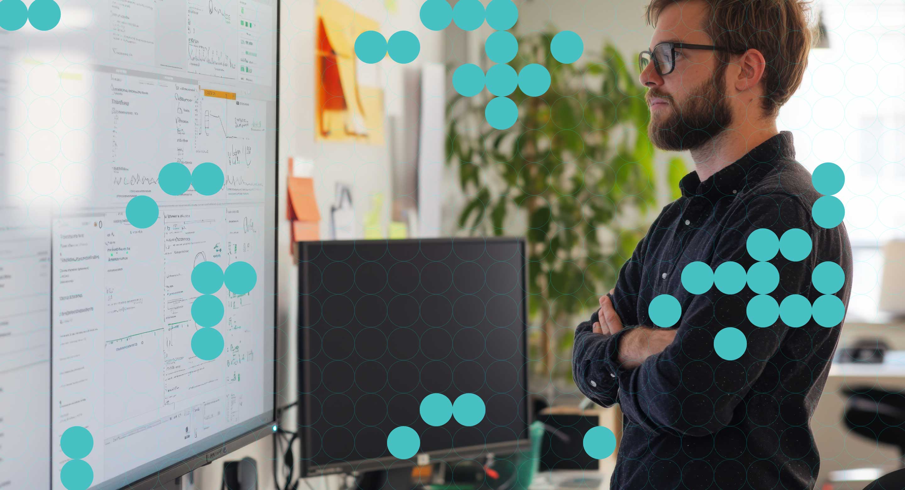 A man with glasses looks thoughtfully at charts and notes on a large screen in an office with a teal circle overlay.