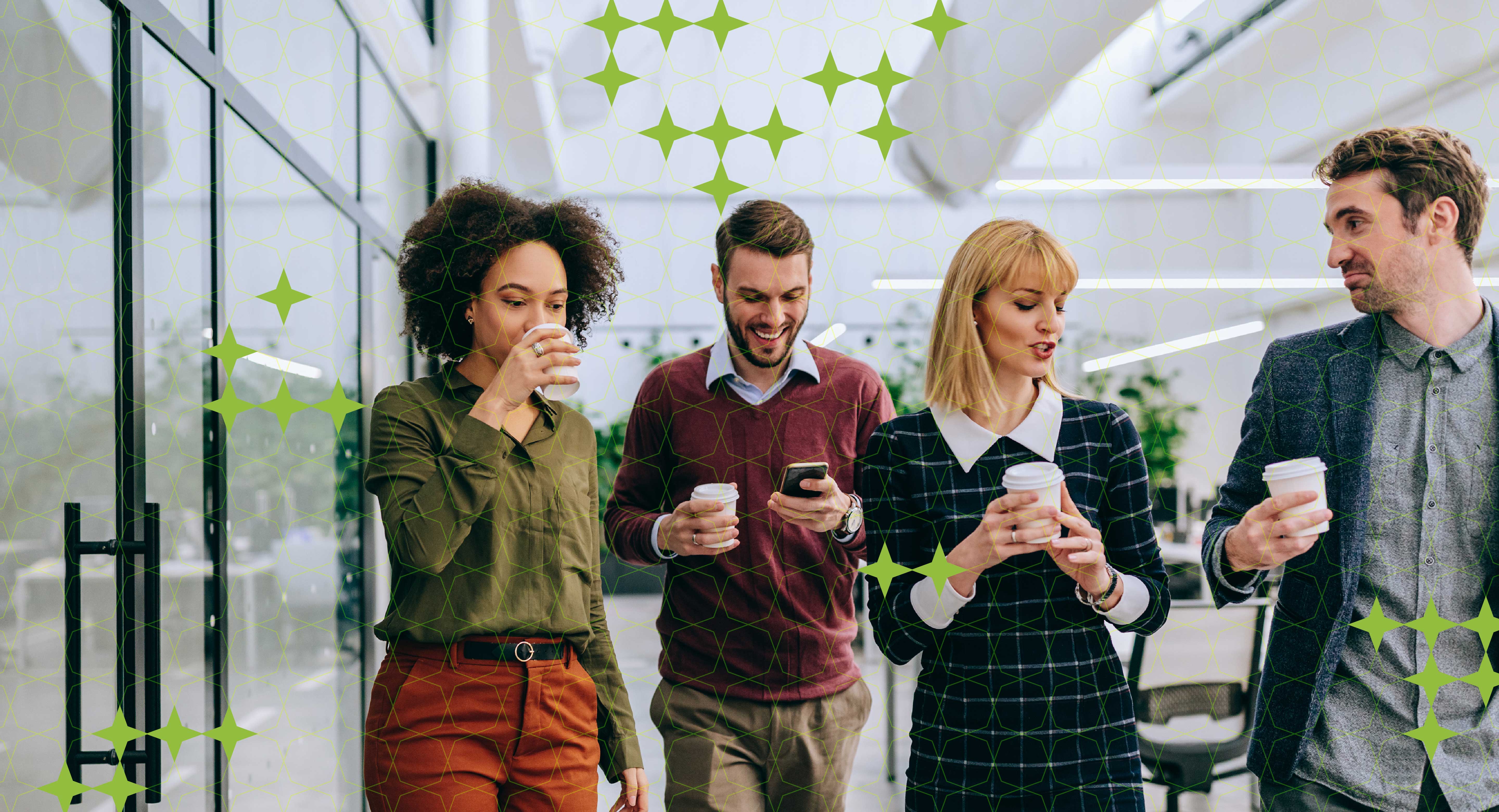 Four co-workers in an office setting chatting and holding coffees.