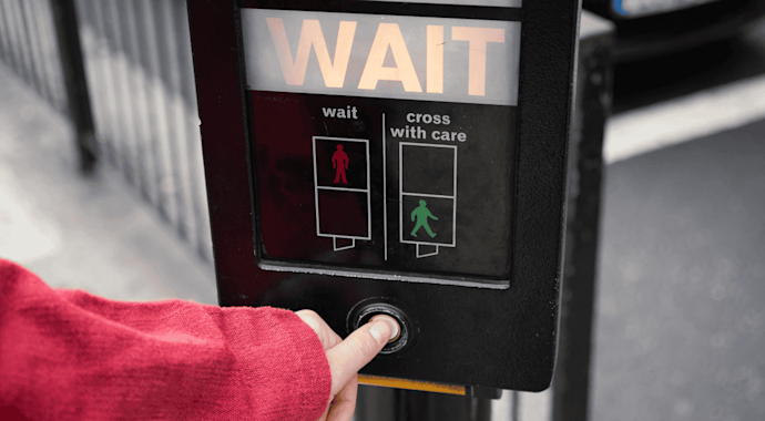 Person pushing a crosswalk button, with the "WAIT" sign lit up