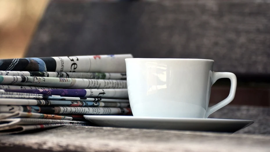 Newspapers stacked on surface next to a mug and saucer