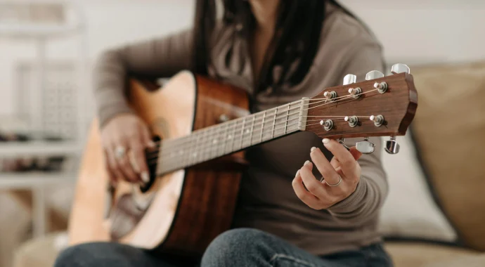 Young woman tuning E-string on acoustic guitar while sitting down on couch