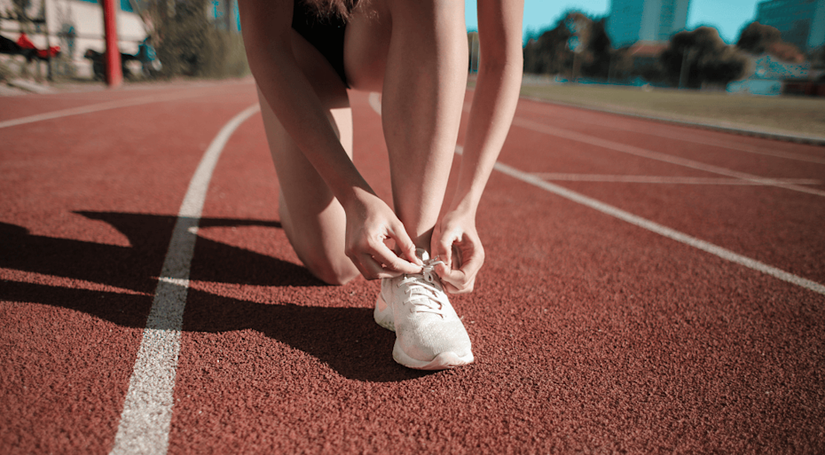 Person tying up their shoelaces on a running track