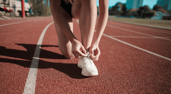 Person tying up their shoelaces on a running track
