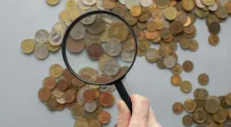 Hand holding magnifying glass over coins