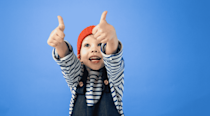 Young kid standing against a blue background giving double thumbs up