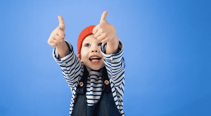 Young kid standing against a blue background giving double thumbs up