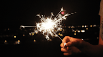 Person holding a sparkler with a backdrop of a dark night sky