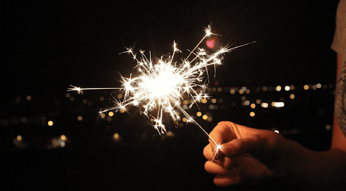 Person holding a sparkler with a backdrop of a dark night sky