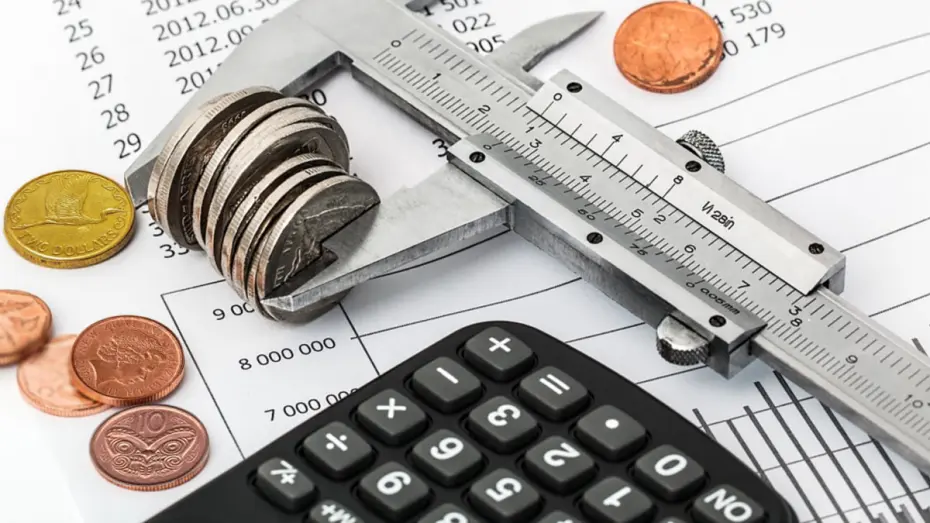 Coins, calculator and ruler sitting on piece of paper with figures on it