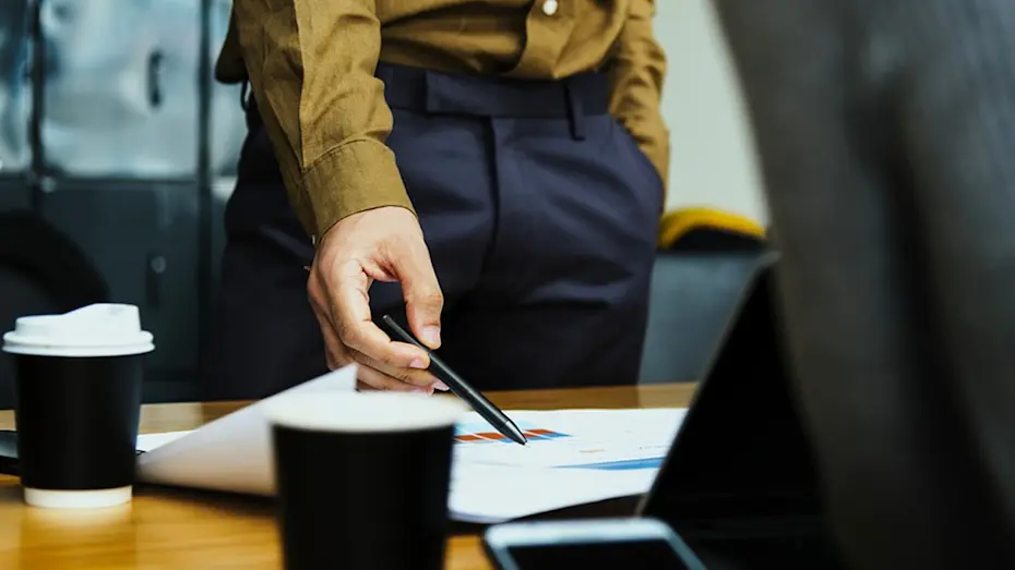 Corporate male holding pen, pointing with pen to graph on table