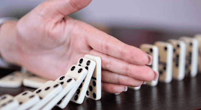 Woman's hand stopping a line of falling dominoes