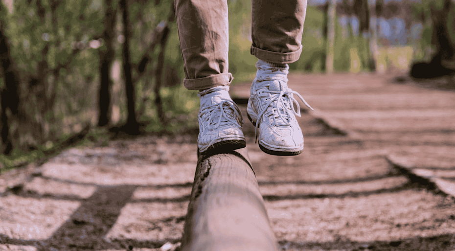 Person balancing walking along a wooden beam in a park