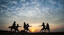 Silhouette of children playing tug of war on a hill, against a sunset
