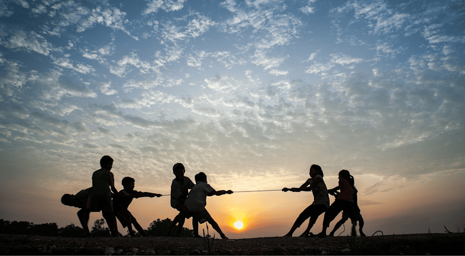 Silhouette of children playing tug of war on a hill, against a sunset