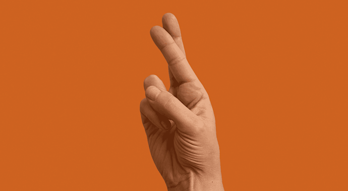 Hand doing crossed fingers signal against an orange background. 