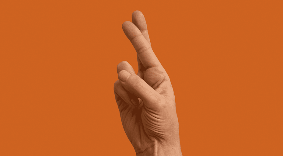 Hand doing crossed fingers signal against an orange background. 