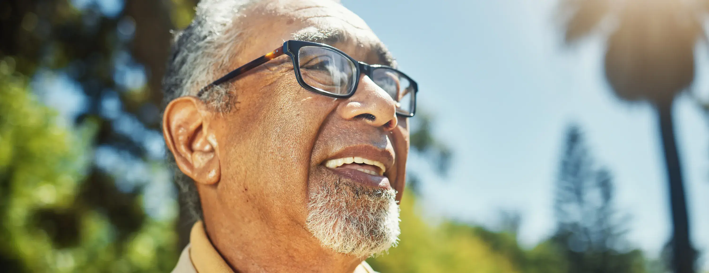 Senior man wearing glasses and smiling with a park background.