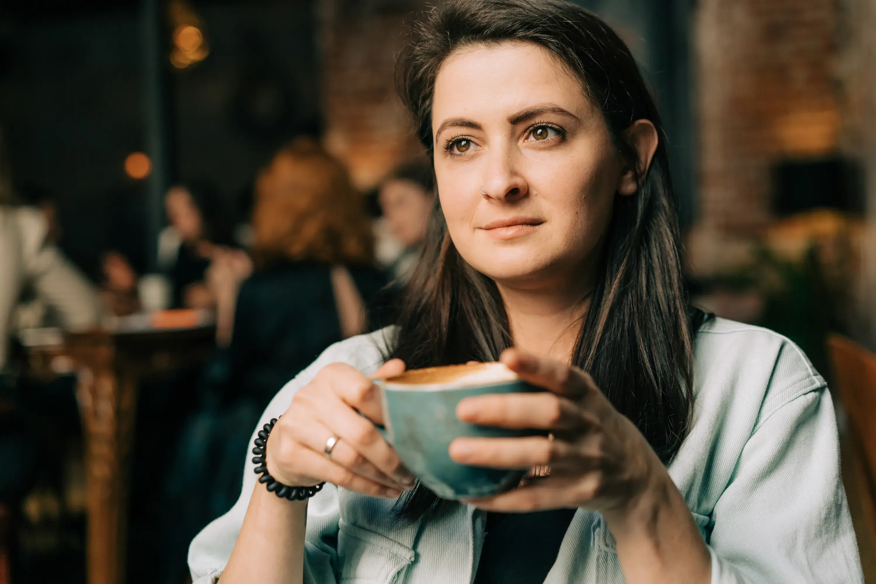 Femme assise qui boit un café d’une tasse dans un décor sombre.