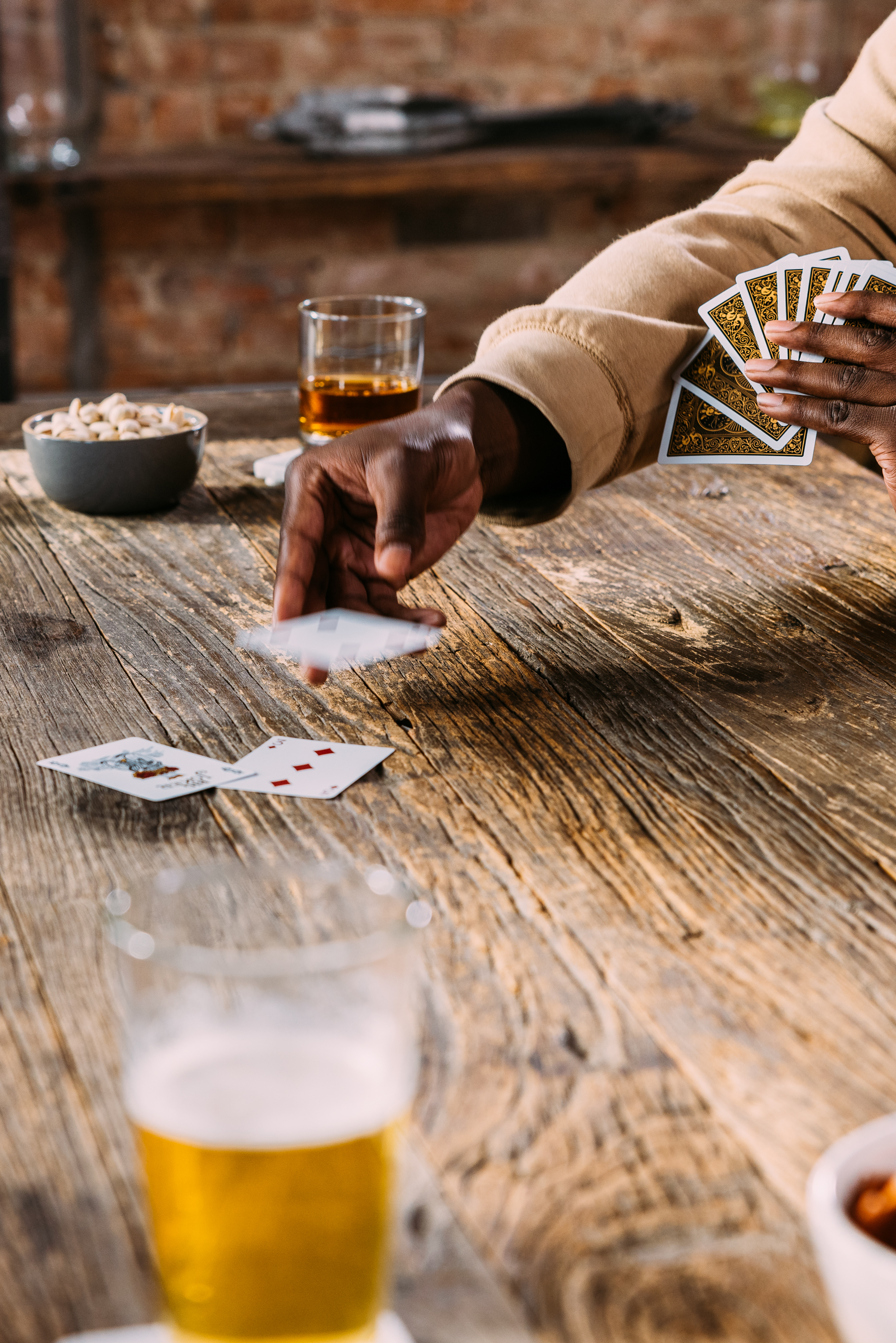 Person throwing down card into play pile on wooden table, with drinks and snacks around.